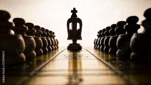Chessboard and silhouettes of figures in the dark against a bright grunge background  the king in the middle and other figures scattered around  the concept of the game and strategy