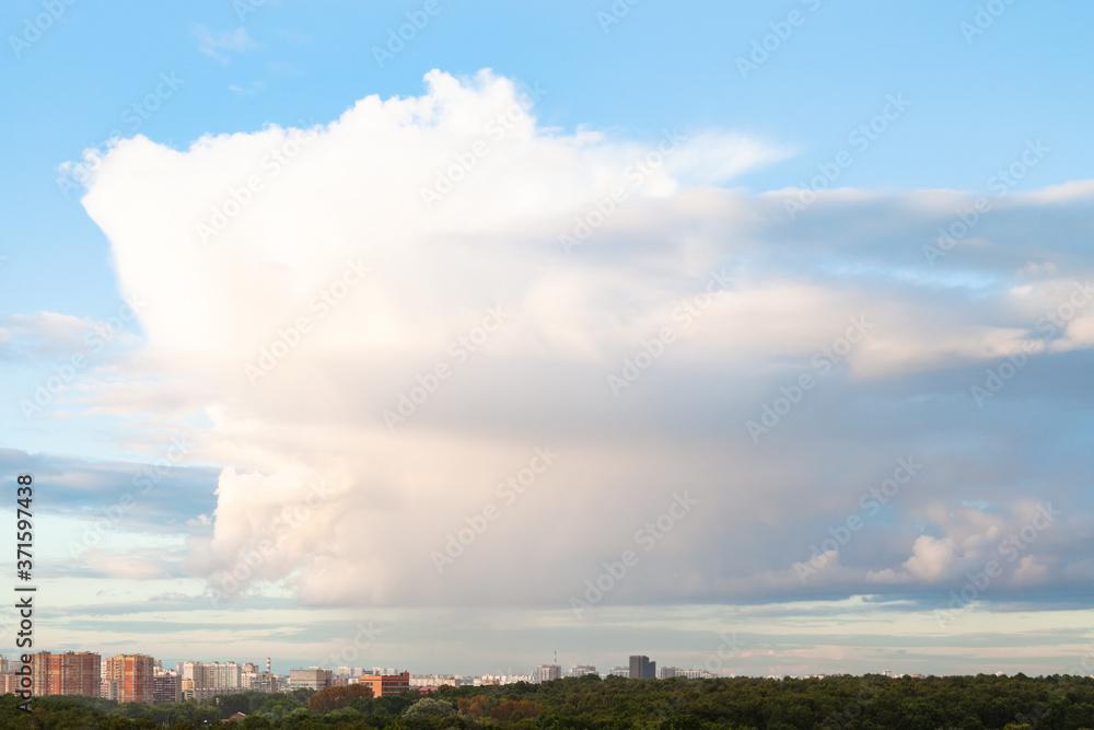 large cloud in blue sky over city and urban park in summer evening