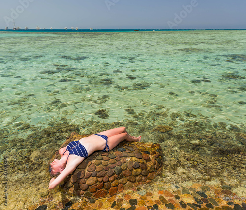 young caucasian blond woman in swim suit over smooth stone suface at summer sea coast view