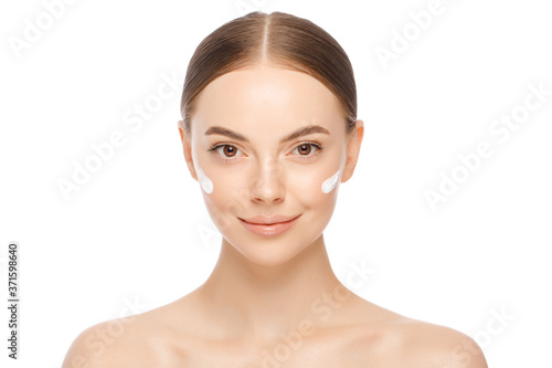 Close-up portrait of young naturally beautiful woman with face cream applied on cheekbones and glowing naked skin, isolated, white background photo