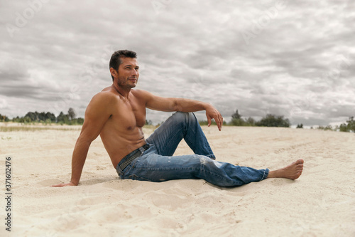 Pensive handsome young man sitting on the dunes in desert © Darya Lavinskaya