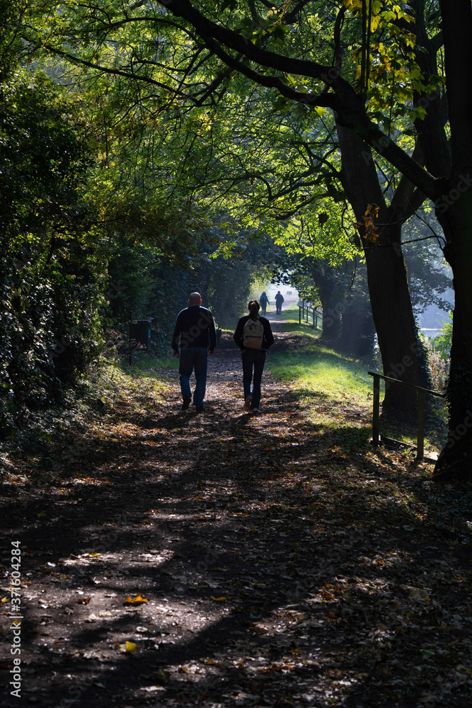 Ramblers Enjoying a Walk Along a Path Covered with Fallen Leaves on a Sunny Autumn Morning Near Ripon Canal, North Yorkshire, England, UK. Ramblers Enjoying a Walk Along a Path Covered with Fallen Leaves on a Sunny Autumn Morning Near Ripon Canal, North Yorkshire, England, UK.