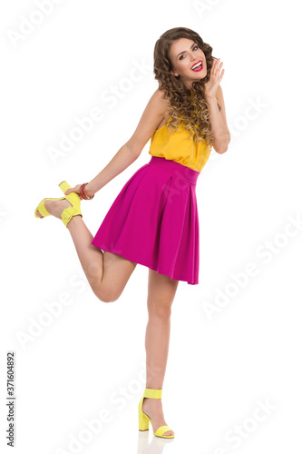 Happy Young Woman In Vibrant Clothes Stands On One Leg And Shoutes