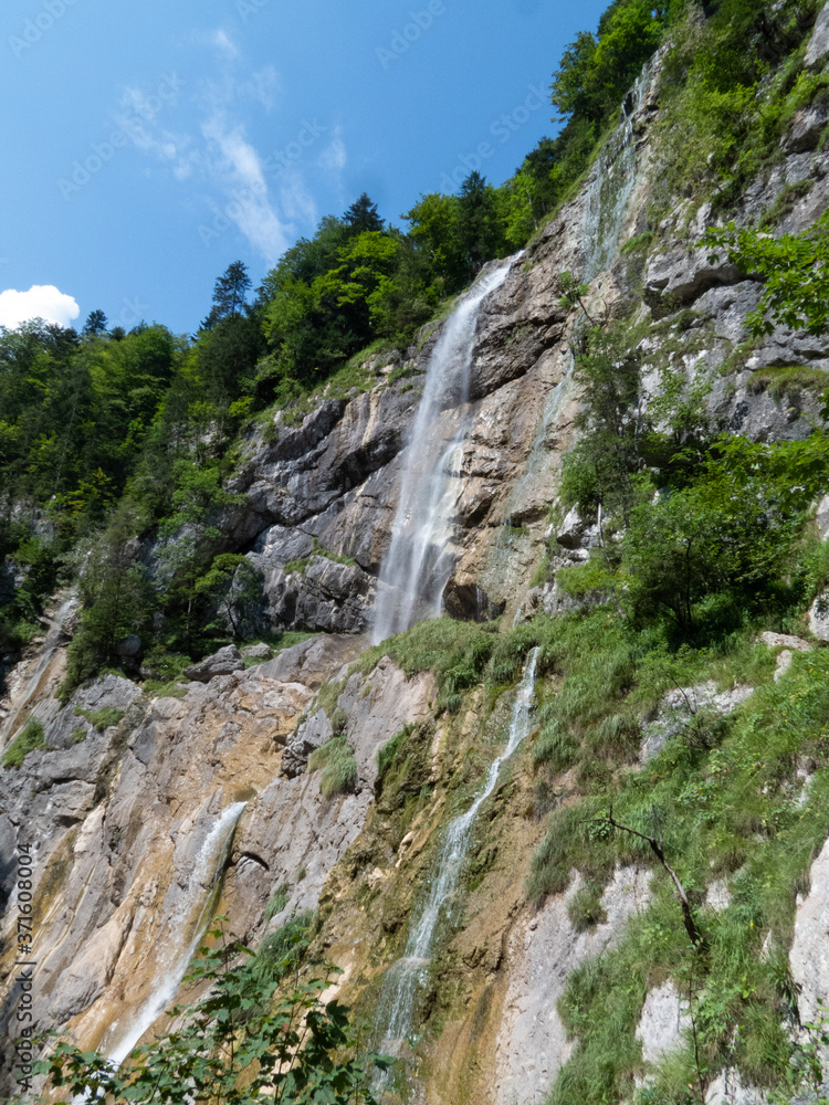 Rock face with waterfall streaming down in the middle, blue sky in background and greenery on sides Rock face with waterfall streaming down in the middle, blue sky in background and greenery on sides
