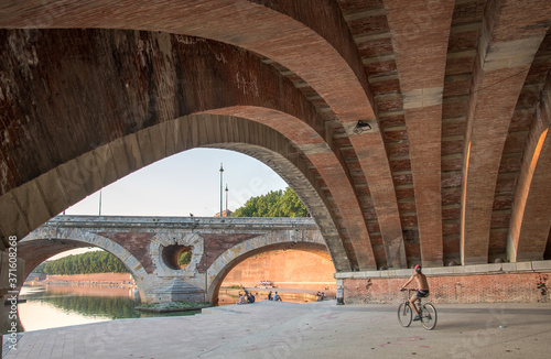 homme faisant du vélo sur des quais et passant sous un vieux pont 