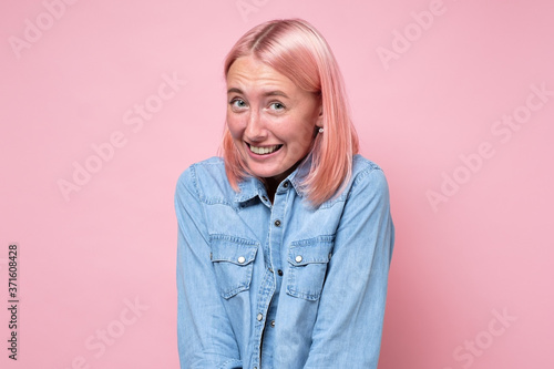 Woman with pink dyed hair smiling looking shy at camera