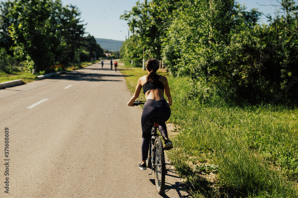 Woman riding bike along asphalt road with green trees on both sides. Woman riding bike along asphalt road with green trees on both sides.
