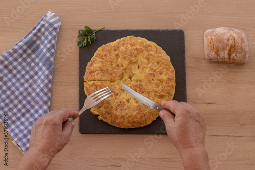 Manos con tenedor y cuchillo preparadas para comerse una tortilla de patatas photo