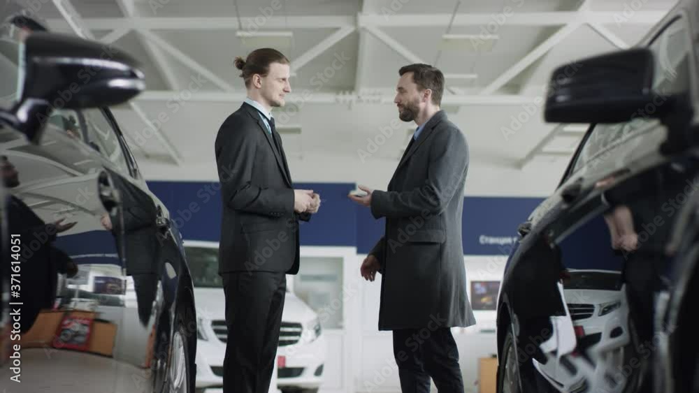 The auto dealership manager gives the key to potential a buyer. The dealer and the customer are shaking hands in the auto showroom. The auto dealership manager gives the key to potential a buyer. The dealer and the customer are shaking hands in the auto showroom.