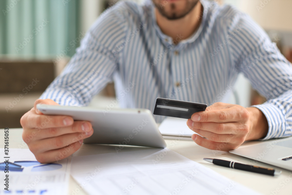 Young man sitting in office and pays by credit card with his tablet. Young man sitting in office and pays by credit card with his tablet.