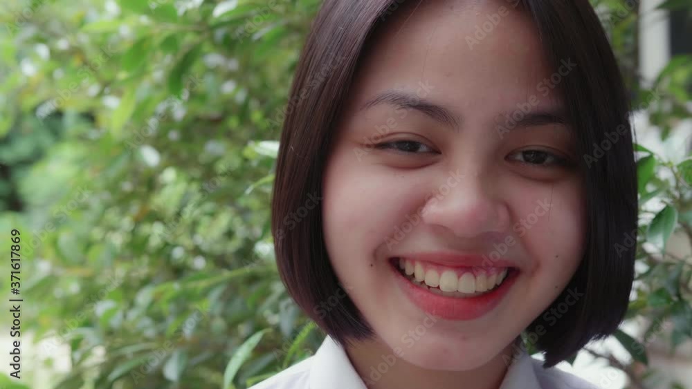 Slow motion of smiling and laughing  Asian teen high school girl in white uniform relaxing in the park.