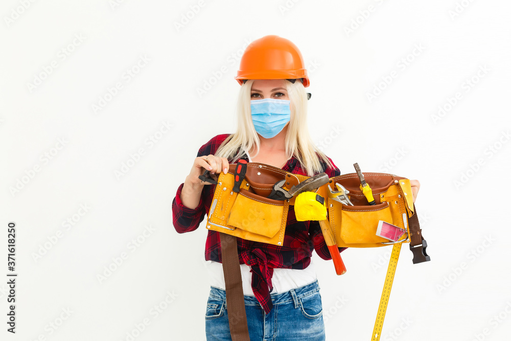 Builder girl in respiratory mask in denim overalls and a cap posing on a white background