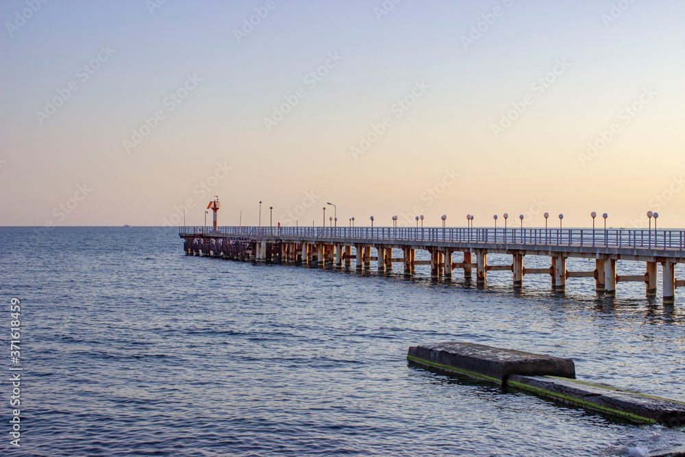 Sea in the evening. The pier goes off into the distance. Dark blue sky and water.Concrete blocks and breakwaters are visible.