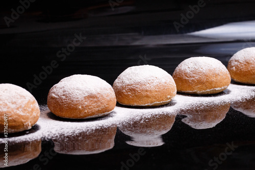Baking on a black background. White buns sprinkled with powder and flour.