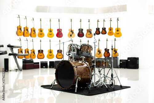 Brown drum set with blurry many guitar on white background in music show room of music shop.