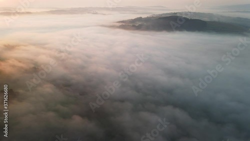 Flying Over Dense Fog and Mist in Countryside. Hills and Forest Above Fog. Early Morning in Late Summer. Sunrise over Wilderness. Drone Aerial Footage Flying Backwards.