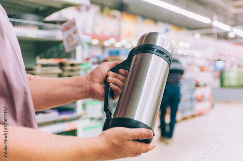 A man in a supermarket holds a thermos in his hands.