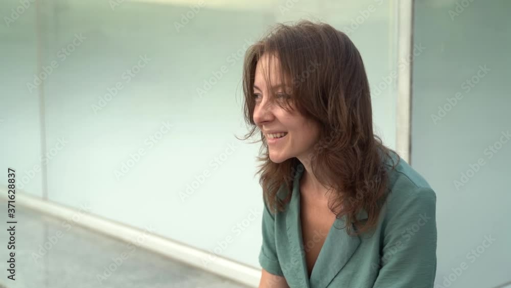 Portrait of a middle-aged woman in a dress sitting outside a building on the street. She enjoys and poses. Portrait of a middle-aged woman in a dress sitting outside a building on the street. She enjoys and poses.