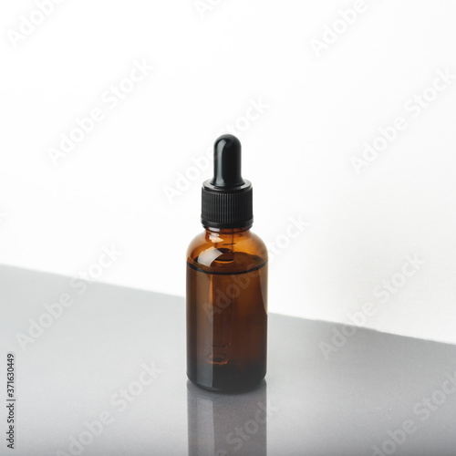 A glass dropper bottle with a pippette with black rubber tip on the grey reflective background. Nature Skin concept. Organic Spa Cosmetics. Close up.