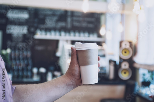 mock-up of a cardboard glass for coffee in a man's hand against the background of a bar in a cafe.