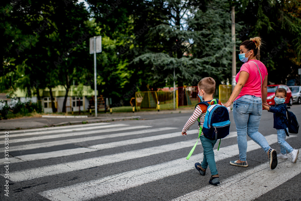Fototapeta premium Mother and children going to preschool during corona virus. Surgical mask for illness prevention.