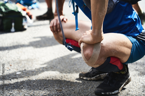 男性のトレイルランナーがトレーニングの前にストレッチしている姿。膝をキネシオテープでテーピング。