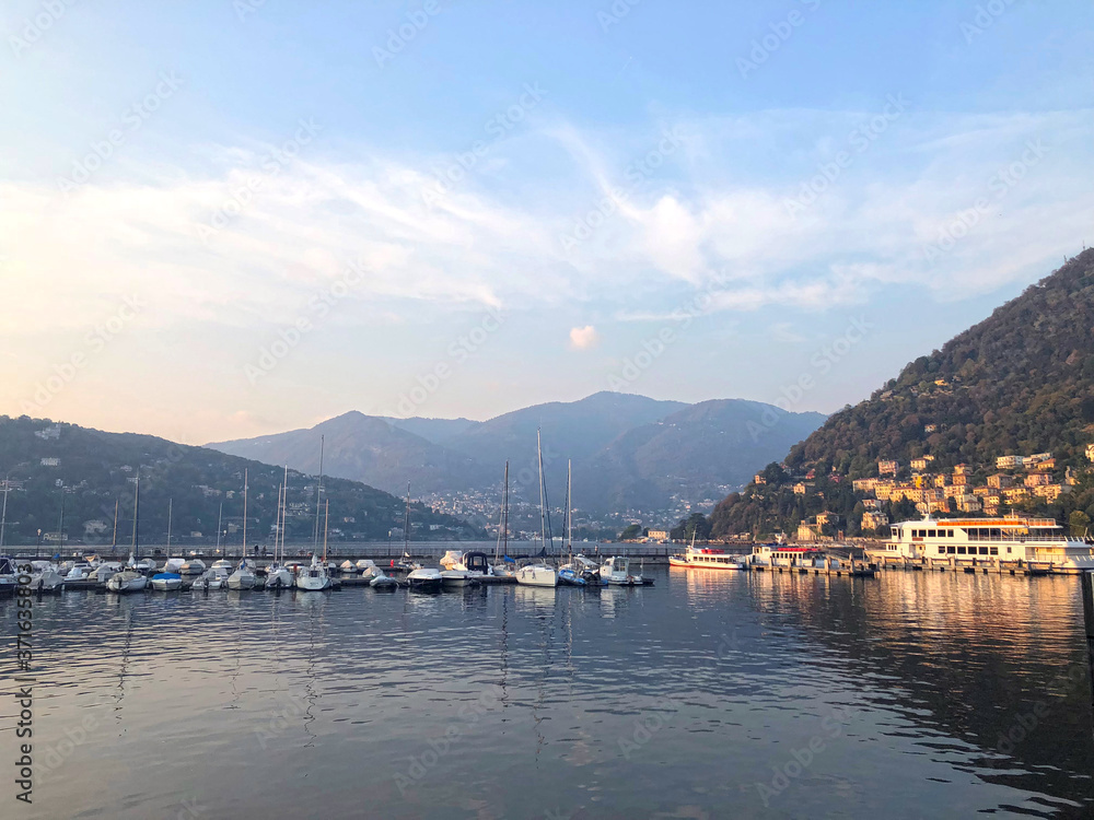 Como Lake, Italy - hills, mountains and water view. Boats and yachts at the marina. Calming autumnal scene, sunset landscape in soft colors