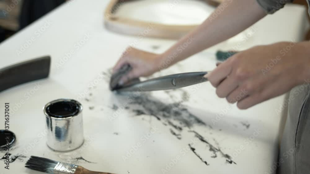 A female restorer polishing a black wooden detail, female hands renew old wooden furniture. Carpenter working with wooden material in workshop A female restorer polishing a black wooden detail, female hands renew old wooden furniture. Carpenter working with wooden material in workshop