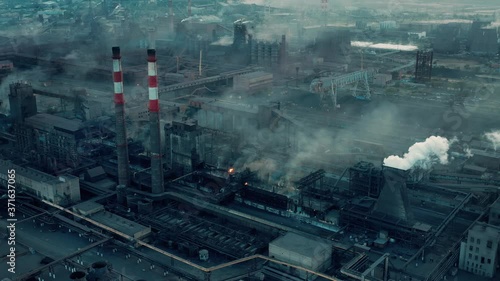 Drone aerial shot factory tubes and chimneys. Fly over zoom in industrial zone, grey and foggy sky, health risk area. Environmental problems, fossil fuels