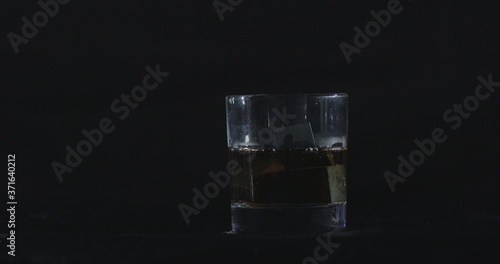 In front of a black background, whiskey is poured into a glass of whiskey stones.