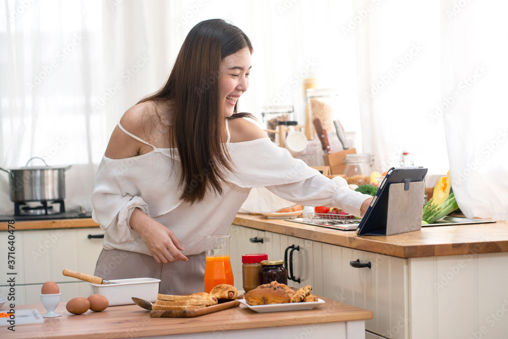 Young Asian woman prepare for breakfast in kitchen, using digital tablet computer Young Asian woman prepare for breakfast in kitchen, using digital tablet computer
