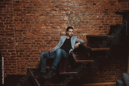 Portrait of a handsome stylish man posing in loft studio interior while lying on wooden stairs. Fashion for men.