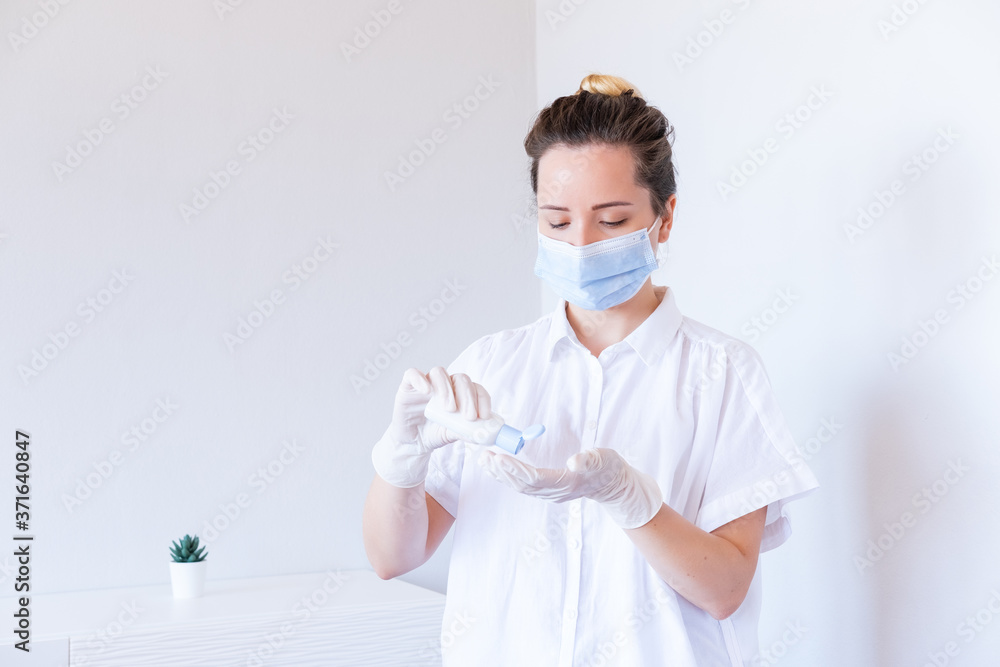 Female doctor in white uniform and protective mask sanitize disinfect hands on medical glove on hospital interior. Medicare. Health care. Female doctor in white uniform and protective mask sanitize disinfect hands on medical glove on hospital interior. Medicare. Health care.