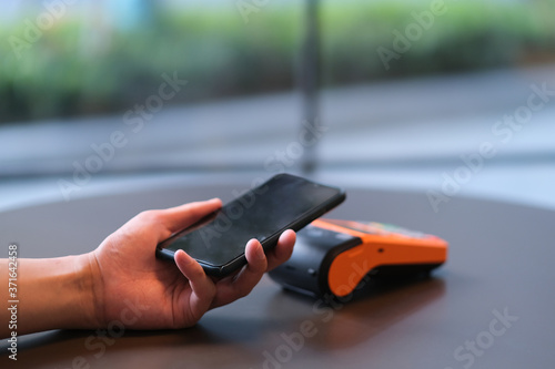 close up hand holding smartphone over pos terminal on table. blur background