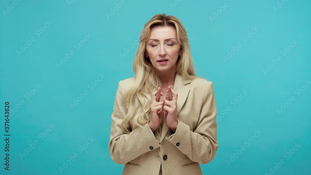Nervous excited adult blond woman in business style suit crossing fingers dreaming about victory, sincerely rejoicing when winning, success symbol. Indoor studio shot isolated on blue background Nervous excited adult blond woman in business style suit crossing fingers dreaming about victory, sincerely rejoicing when winning, success symbol. Indoor studio shot isolated on blue background