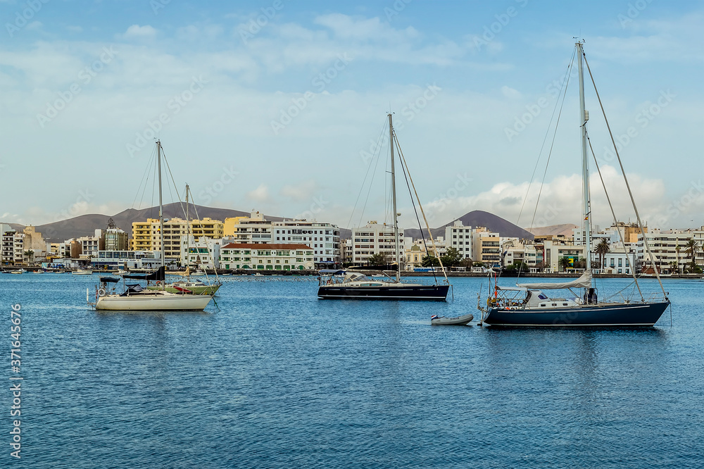 A close up of yachts moored in a sheltered bay with the backdrop of the shoreline of Arrecife, Lanzarote on a sunny afternoon
