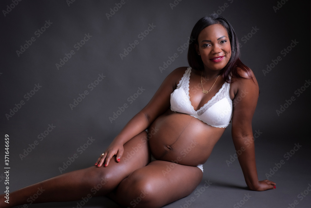 Foto de Mujer de raza negra embarazada en ropa interior blanca sentada do  Stock