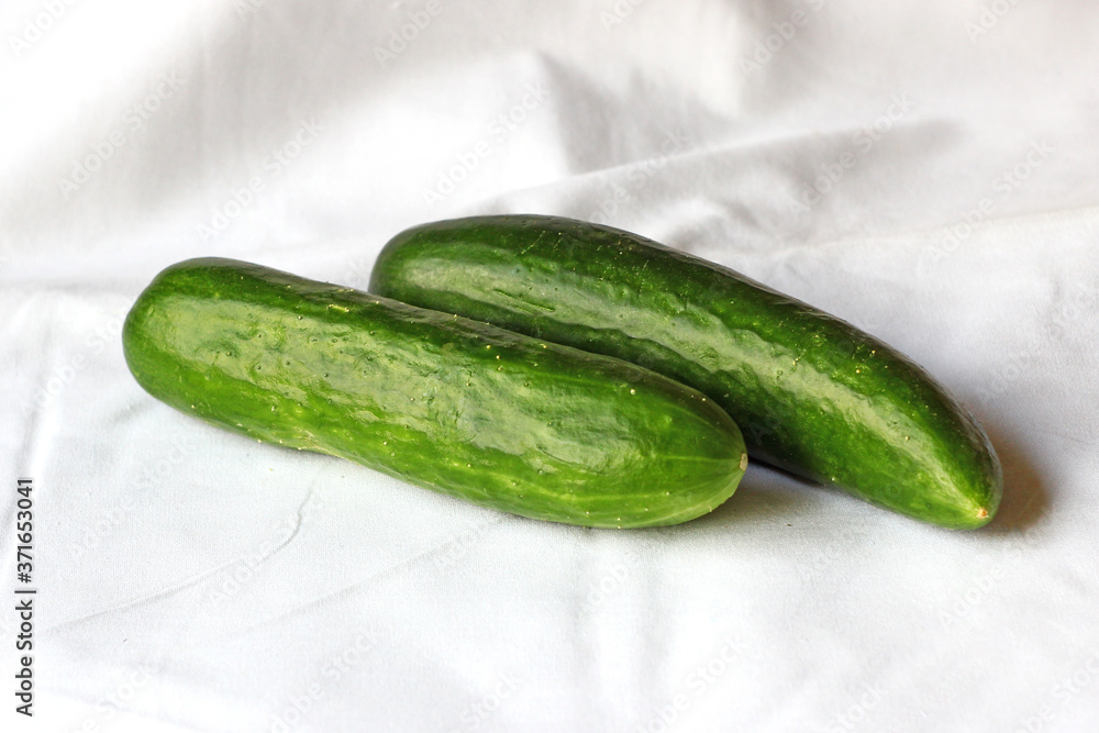 Close up of two cucumbers on white fabric Close up of two cucumbers on white fabric