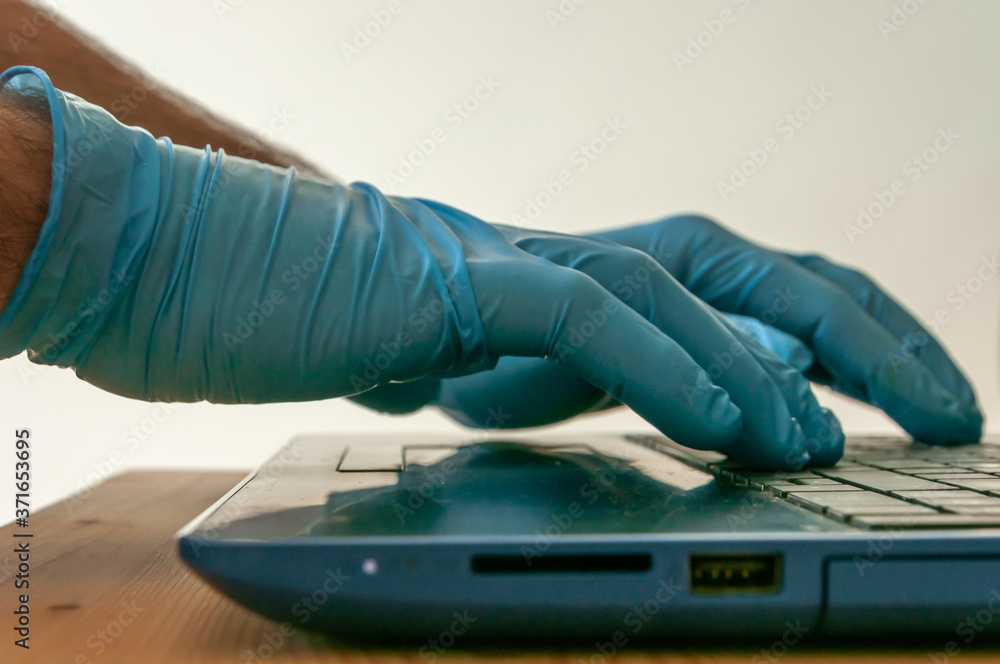 Hands with blue nitrile gloves using a labtop keyboard