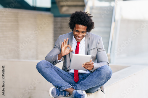 Black Businessman using a digital tablet sitting near an office building.