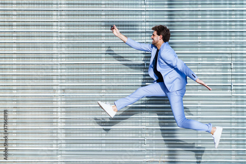 Man wearing a suit makes a selfie with a smartphone while jumping