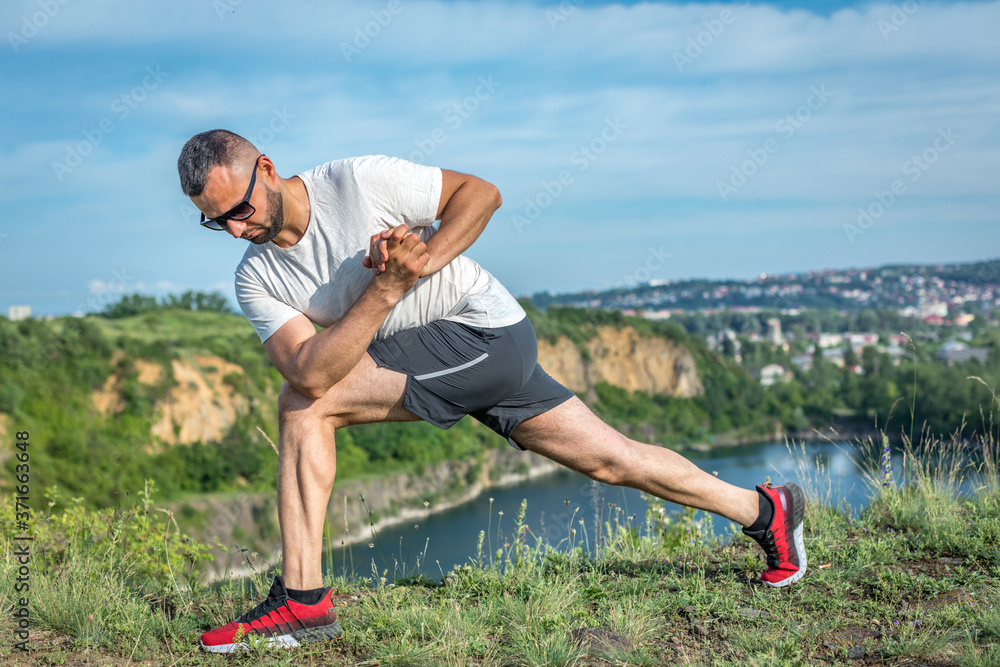 Professional fitness trainer. Bearded sportsman is training himself, makes streching at the quarry lake. Outdoors workout fitness concept. Professional fitness trainer. Bearded sportsman is training himself, makes streching at the quarry lake. Outdoors workout fitness concept.