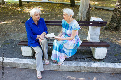 The two elderly women together in a summer park with newspaper. photo