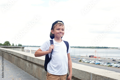 A boy of European appearance in a white t shirt and with a backpack goes and laughs with happiness