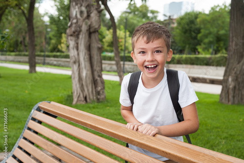 A boy of European appearance in a white t shirt and with a backpack walks in the Park and laughs