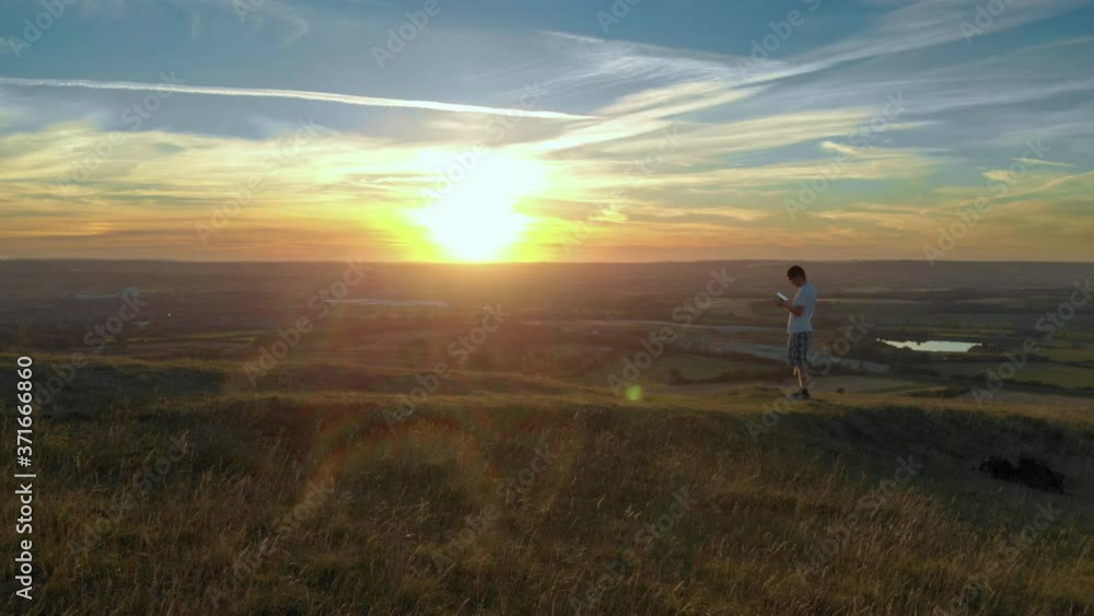 Drone pilot on mountain peak using remote controller during vivid sunset Drone pilot on mountain peak using remote controller during vivid sunset