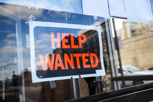 Reflection of a man looking at a help wanted sign in a business window, economy concept photo