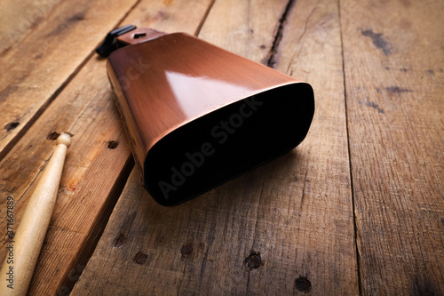 Copper Cowbell musical instrument on a wooden background with drumstick photo