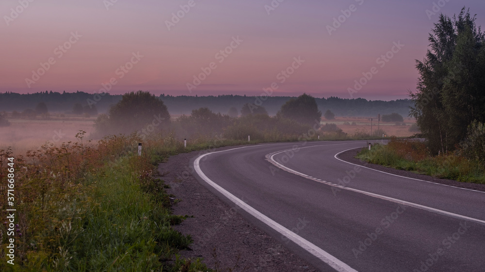 Road between foggy fields at dawn in early autumn in the countryside