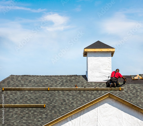 Roofer attaching shingles on a rooftop of a new building photo